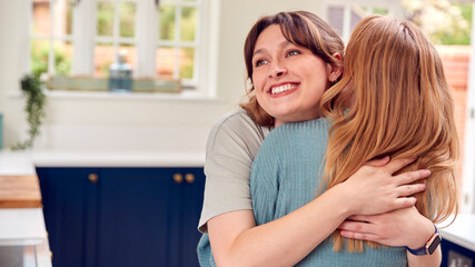 Fototapeta premium Two Female Friends Greeting And Hugging In Kitchen At Home