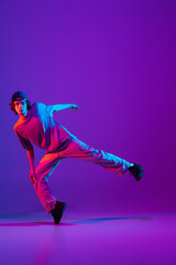 Stylish sportive boy dancing hip-hop in stylish clothes on colorful background at dance hall in...