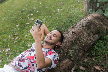 smiling young gay man using cellphone in the park
