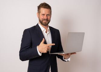 Young business man standing with laptop. Handsome guy holding open notebook in his hand and work on it. Information, technology concept.