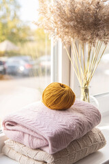 On the windowsill is a stack of sweaters and a ball of yarn. Autumn comfort and creativity.