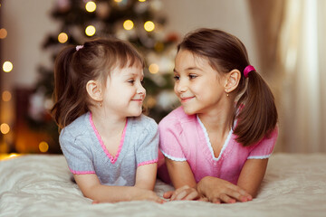 Naklejka premium two smiling girls sisters look at each other against the background of a blurred Christmas tree