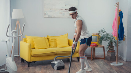 young man in sportswear vacuum cleaning living room, retro sport concept