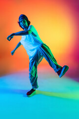 Fototapeta na wymiar Close-up portrait of young man, hip-hop dancer in stylish clothes in action isolated on colorful background at dance hall in neon light.