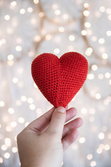 Knitted red heart in the hand against the background of a garland. The concept of love and Valentines Day.