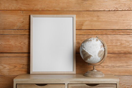 Empty frame with globe on table near wooden wall. Mockup for design