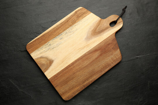 Wooden cutting board on black table, top view. Cooking utensil