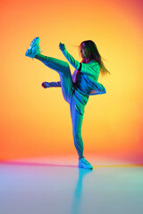 Portrait of young sportive girl dancing hip-hop in stylish clothes on colorful background at dance hall in neon light. Youth culture, movement, style and fashion, action.