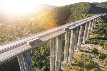Aerial drone view of busy highway viaduct bridge with many cargo transportation trucks driving on