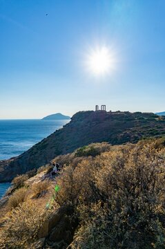 Greek temple on the side of a cliff with the sun in front
