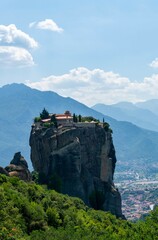 Fototapeta na wymiar Meteora Monastery on top of the rock, with a green forest and a blue sky with white clouds