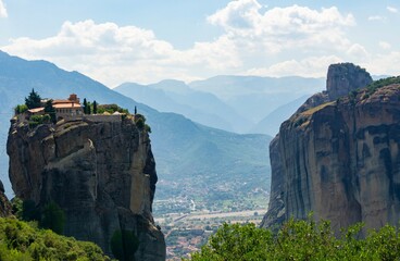 Meteora Monastery on top of the rock, with a green forest and a blue sky with white clouds