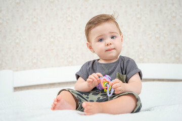 Smiling Caucasian baby boy in shorts and t-shirt playing with colorful rattle toy. Activities for infants. Baby holding a toy.