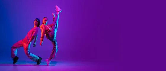 Fotobehang Flyer. Two dancers, young man and woman dancing hip-hop in casual sports youth clothes on gradient purple pink background at dance hall in neon light. © master1305
