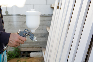 Close-up of a spray gun in a man hand. The process of painting the boards with white paint. Finishing finish. Restoration of old furniture. Compressor operation. Work tool. Fast and easy. Copy space