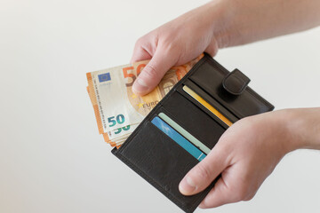 Man's hand holding a black wallet with euro money.