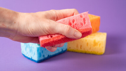 Hand holding red sponge on purple background. Ready for dish wash. Kitchen cleaning sponges