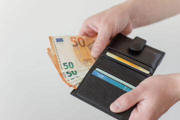 Pay in euros. Get euros from your wallet. Male  hands holding a black leather wallet with 50 euro banknotes and counting them.