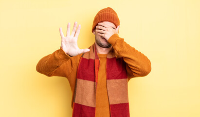 young handsome man covering face with hand and putting other hand up front to stop camera, refusing...