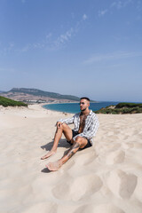 Chico atletico tatuado posando en dunas de arena