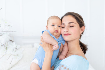 a young mother with a newborn baby gently embraces him at home on the bed, the concept of a happy family and birth