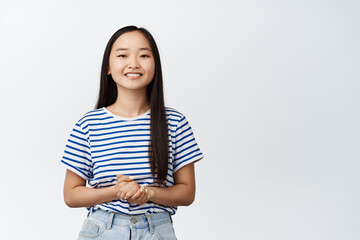 Smiling asian girl looks polite and professional, ready to help and provide assistance, stands against white background - 457108739
