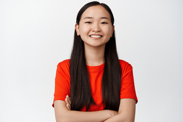 Portrait of young asian female student, smiling and looking happy, cross arms on chest, professional and confident pose, white background