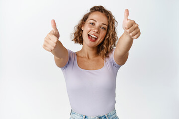 Happy blond girl shows thumbs up and smiling, give praises, complimenting, recommending good...