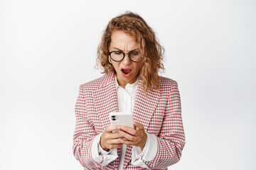 Shocked businesswoman looking at her phone, standing against white background