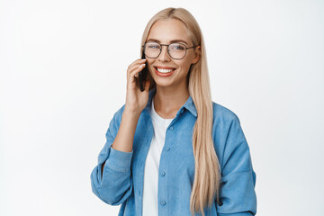 Portrait of smiling blond woman in glasses talking on mobile phone, having a smartphone call, standing against white background
