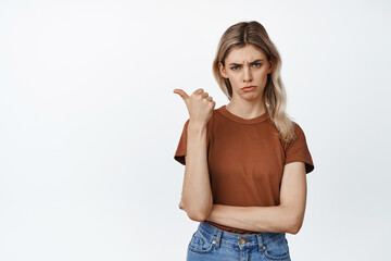 Sad and moody girl pointing left, looking with skeptical face expression, express disappointment, white background