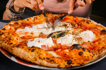 Pizza napoletana con ricotta, pomodoro e basilico fresco mentre viene tagliata con forchetta e coltello
