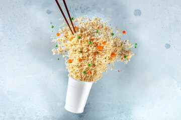 Ramen cup with instant noodles flying out of it and chopsticks, fast food levitation. Noodle meal...