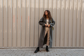Pretty young stylish woman model with curly hair in a fashionable long coat with boots straightens...