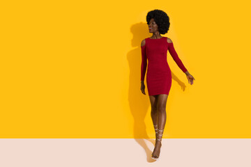 Fototapeta na wymiar Happy Young Black Woman In Red Mini Dress And High Heels Is Walking Towards Camera And Looking Away