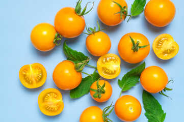 Ripe fresh yellow orange tomatoes with green tails, leaves on blue background flat lay top view. Cherry tomatoes. Vegetables, healthy vegan organic food, harvest concept, tomatoes pattern, cooking