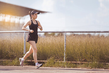 Happy smiling adult Asian woman jogging outdoor in the city park in sunshine beautiful summer day.  Happy relaxed mature woman jogging to live an active and healthy lifestyle