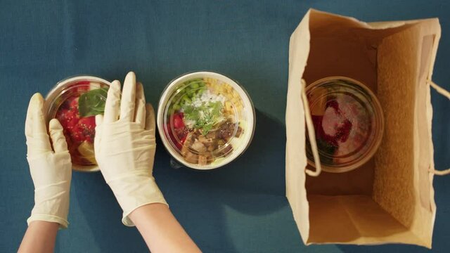 Food delivery of traditional Hawaiian cuisine. Packaging cooked poke bowls into paper bag, wearing protective gloves. Healthy vegetarian eating. Asian vegan raw meal. Delivery services during covid.