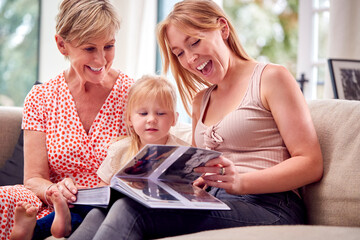 Grandmother Sitting On Sofa With Adult Daughter And Granddaughter At Home Looking At Photo Album