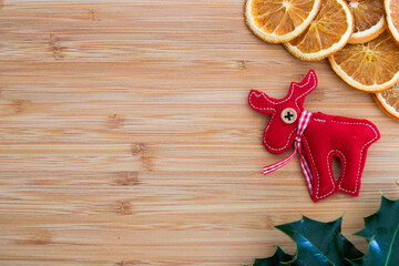 Flat lay of red felt reindeer christmas decoration, with orange slices and holly leaves, on wooden...