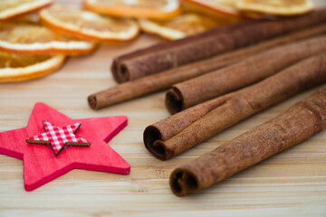 Cinnamon sticks, red wooden christmas decoration star and dried oranges in the background, close up on wooden surface