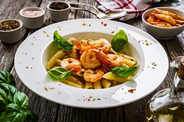 Penne with fried prawns on wooden background
