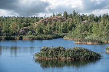 A lake with a plane surface and reflections against the blue sky and white clouds. Originated from an old quarry flooded, groups of islands overgrown with reeds.