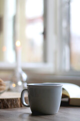 Bowl of cookies, cup of hot beverage, open book and lit candles on a table. Selective focus.