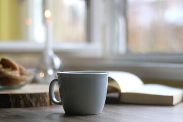 Bowl of cookies, cup of hot beverage, open book and lit candles on a table. Selective focus.