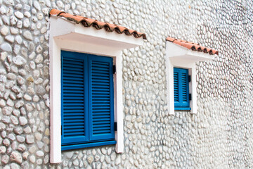 Fototapeta na wymiar Herceg Novi, Montenegro, August 30, 2018. Two wooden windows with blue shutters in a stone house