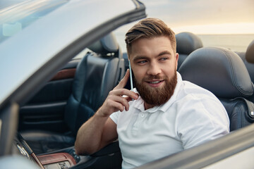 Young man talking on mobile phone in cabriolet car