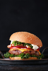 Fast food. Burger with beef, cheese, bacon and vegetables: tomato, onion, cabbage and sauce on a black plate on a black table. Background image, copy space