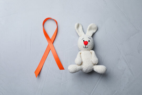Orange ribbon and toy bunny on light grey table, flat lay. Multiple sclerosis awareness