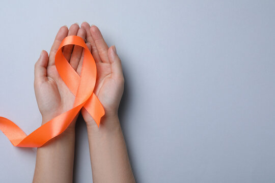 Woman holding orange ribbon on light grey background, top view with space for text. Multiple sclerosis awareness